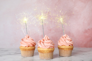 Image of Birthday cupcakes with sparklers on table against light pink background