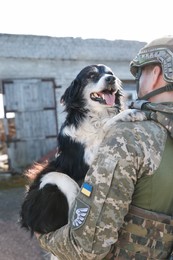 Photo of Ukrainian soldier rescuing stray dog outdoors, back view