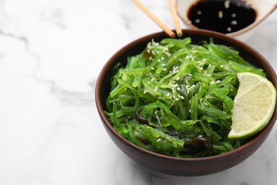 Photo of Tasty seaweed salad in bowl served on white marble table, closeup. Space for text