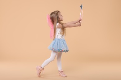 Photo of Cute little girl in fairy costume with pink wings and magic wand on beige background