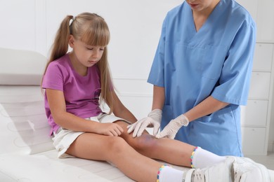 Photo of Doctor examining little girl's bruised knee in hospital
