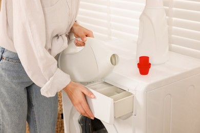 Photo of Woman pouring laundry detergent into washing machine indoors, closeup