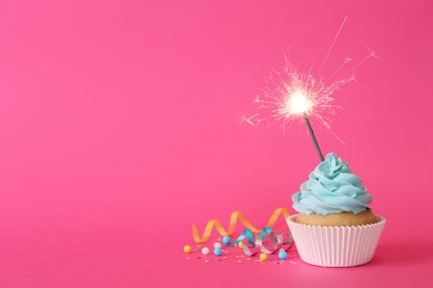 Photo of Birthday cupcake with burning sparkler and streamers on pink background. Space for text