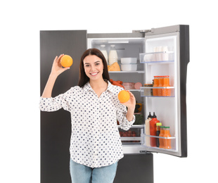Photo of Young woman with oranges near open refrigerator on white background