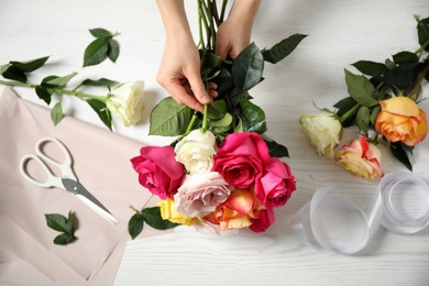 Photo of Woman making luxury bouquet of fresh roses at white wooden table, top view