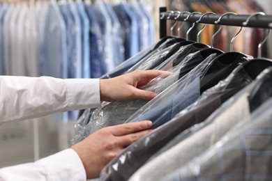 Photo of Dry-cleaning service. Woman taking jacket in plastic bag from rack indoors, closeup