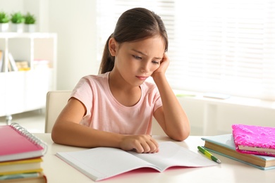 Photo of Sad little girl doing homework at table indoors