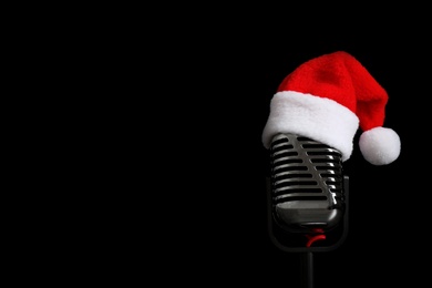 Photo of Microphone with Santa hat on black background, space for text. Christmas music