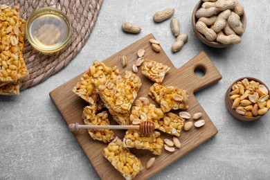 Photo of Delicious peanut kozinaki bars, nuts and honey on light gray textured table, flat lay