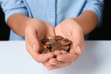 Photo of Young woman holding pile of coins at white table, closeup view