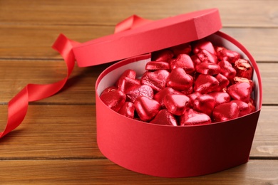 Photo of Box of heart shaped chocolate candies and ribbon on wooden table