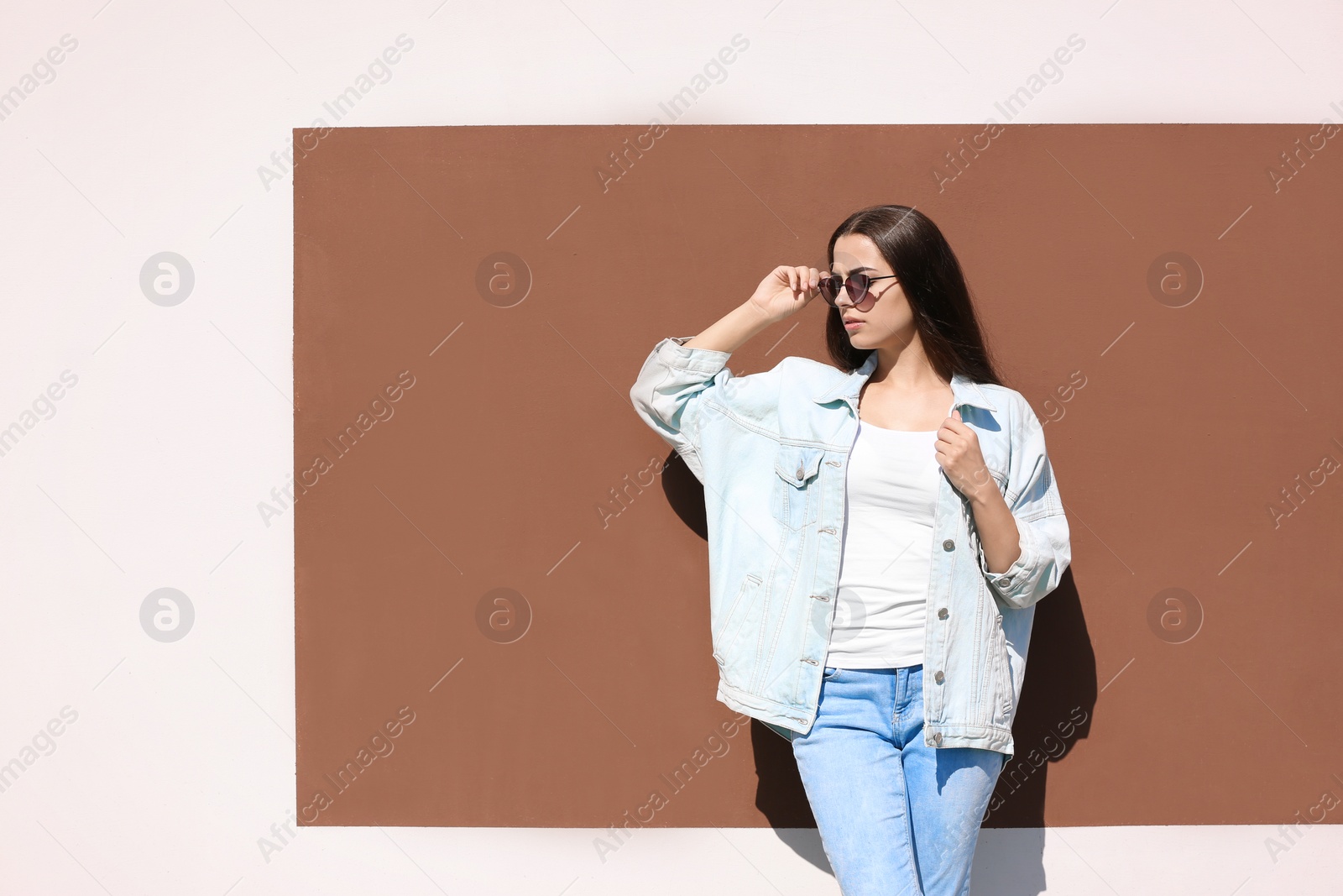 Photo of Young hipster woman in stylish jeans and jacket posing near color wall