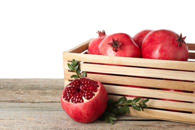 Photo of Fresh pomegranates in crate and green leaves on wooden table against white background