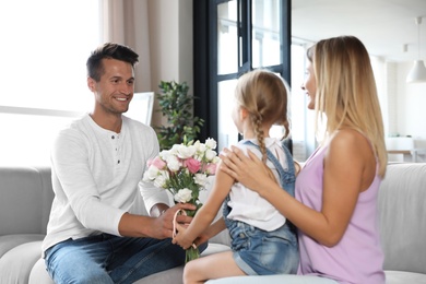 Photo of Young man congratulating his wife and daughter in living room