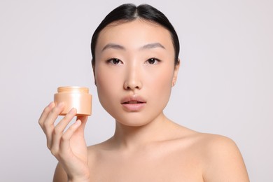 Photo of Beautiful young Asian woman holding jar of body cream on light grey background