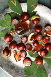 Photo of Chestnuts, leaves and bottles of essential oil on silver plate, top view