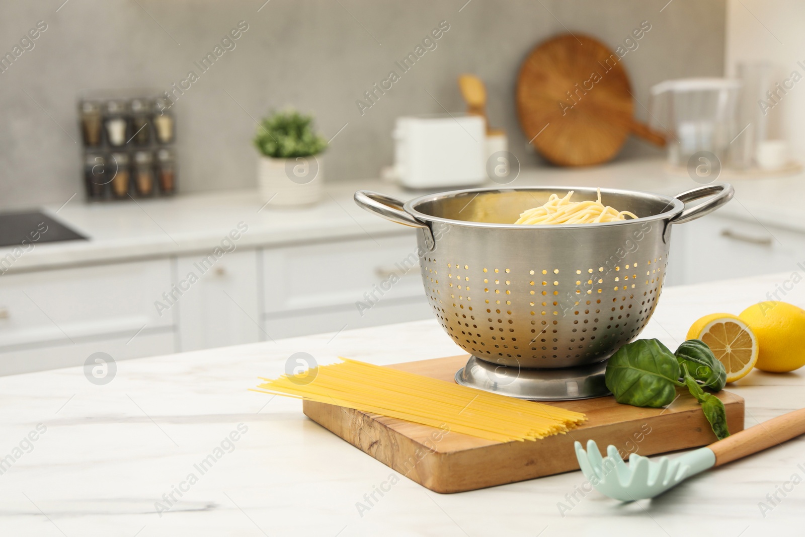 Photo of Cooked pasta in metal colander and products on white marble table in kitchen. Space for text