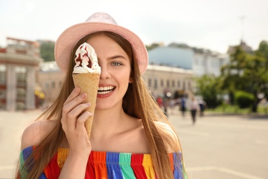 Photo of Young happy woman with ice cream cone on city street. Space for text