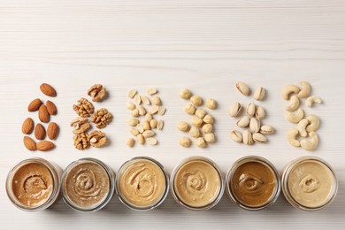 Photo of Many tasty nut butters in jars and nuts on white wooden table, flat lay. Space for text