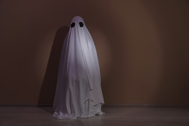 Photo of Creepy ghost. Woman covered with sheet near brown wall. Space for text