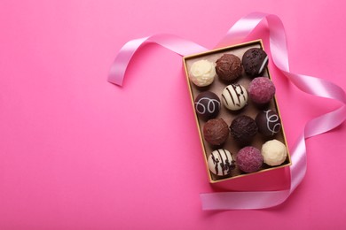 Photo of Open box with delicious chocolate candies and ribbon on pink background, top view. Space for text