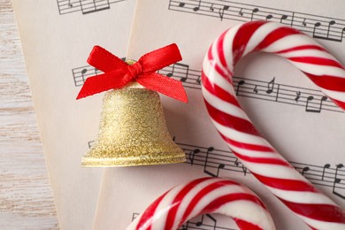 Photo of Golden shiny bell with red bow, music sheets and candy canes on wooden table, flat lay. Christmas decoration