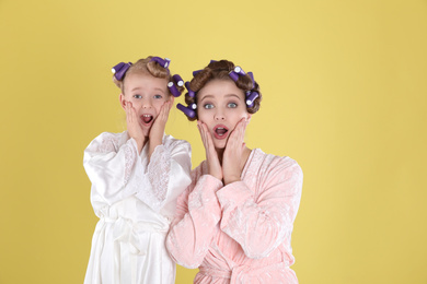 Photo of Emotional mother and daughter with curlers on yellow background