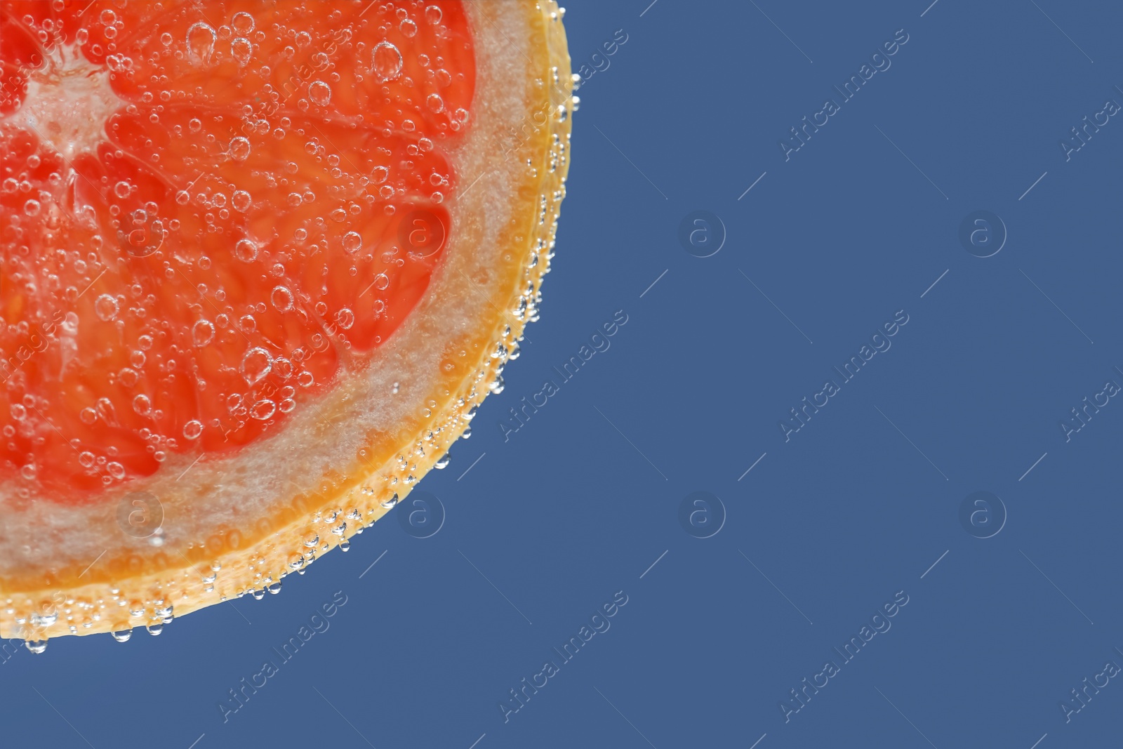 Slice of grapefruit in sparkling water on blue background, closeup with space for text. Citrus soda Photo of Slice of grapefruit in sparkling water on blue background, closeup with space for text. Citrus soda