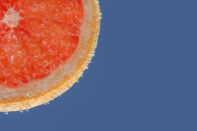 Photo of Slice of grapefruit in sparkling water on blue background, closeup with space for text. Citrus soda