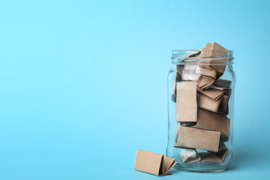 Photo of Glass jar full of brown paper sheets on light blue background, space for text