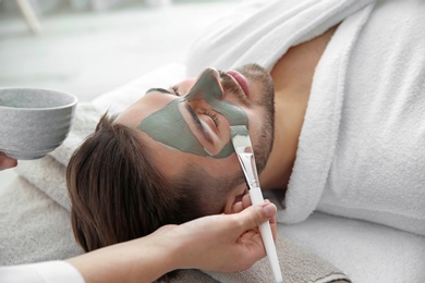 Photo of Cosmetologist applying mask on client's face in spa salon