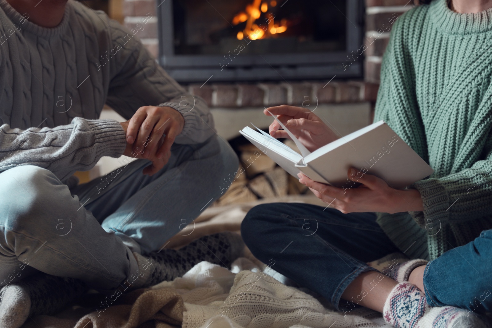 Photo of Couple reading book near burning fireplace at home, closeup