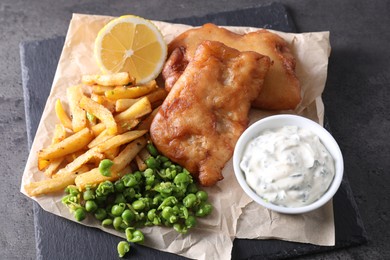Photo of Tasty fish, chips, sauce and peas on grey table, above view