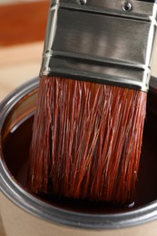 Photo of Dipping brush into can with wood stain on table, closeup