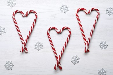Photo of Hearts made of sweet Christmas candy canes and snowflakes on white wooden table, flat lay
