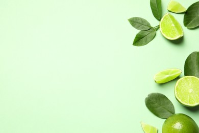 Photo of Whole and cut fresh ripe limes with leaves on light green background, flat lay