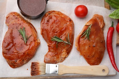 Photo of Raw marinated meat, rosemary, products and basting brush on table, flat lay