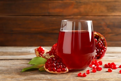 Photo of Glass of pomegranate juice and fresh fruits on table against wooden background, space for text