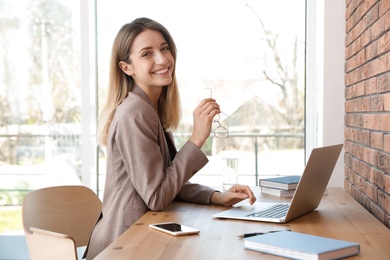 Photo of Young businesswoman using laptop at table in office