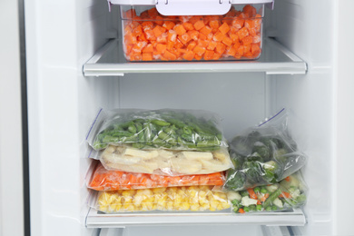 Photo of Plastic bags and containers with different frozen vegetables in refrigerator