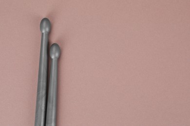 Photo of Two gray drum sticks on dusty rose background, top view. Space for text