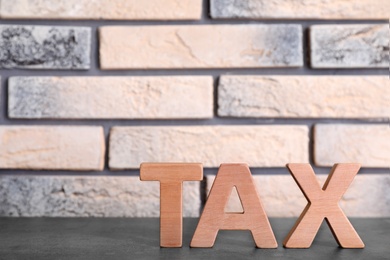 Photo of Word Tax made of letters on wooden table against brick wall