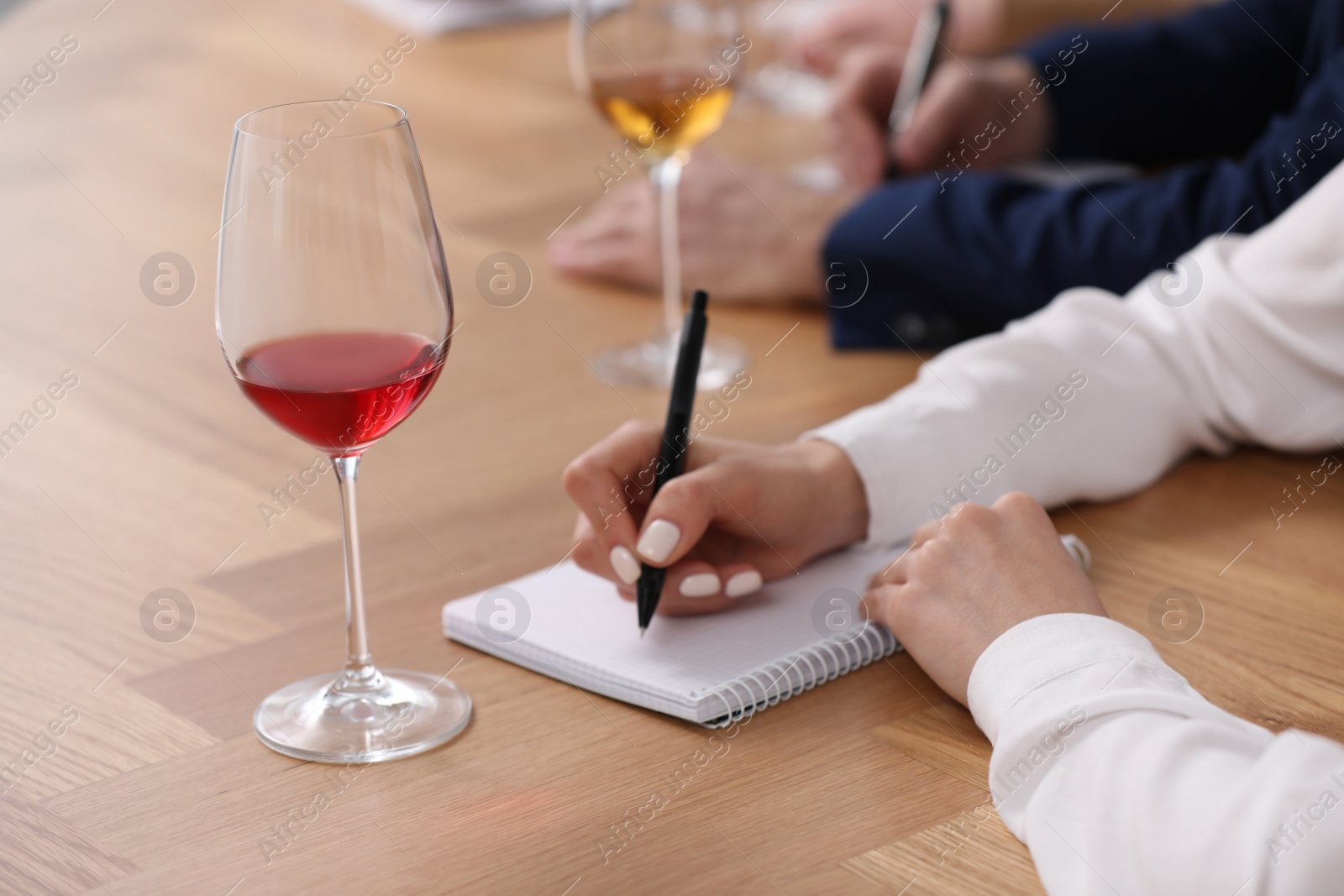 Photo of Sommeliers making notes during wine tasting at table indoors, closeup