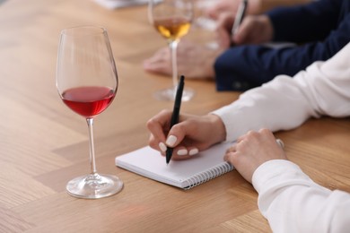 Photo of Sommeliers making notes during wine tasting at table indoors, closeup