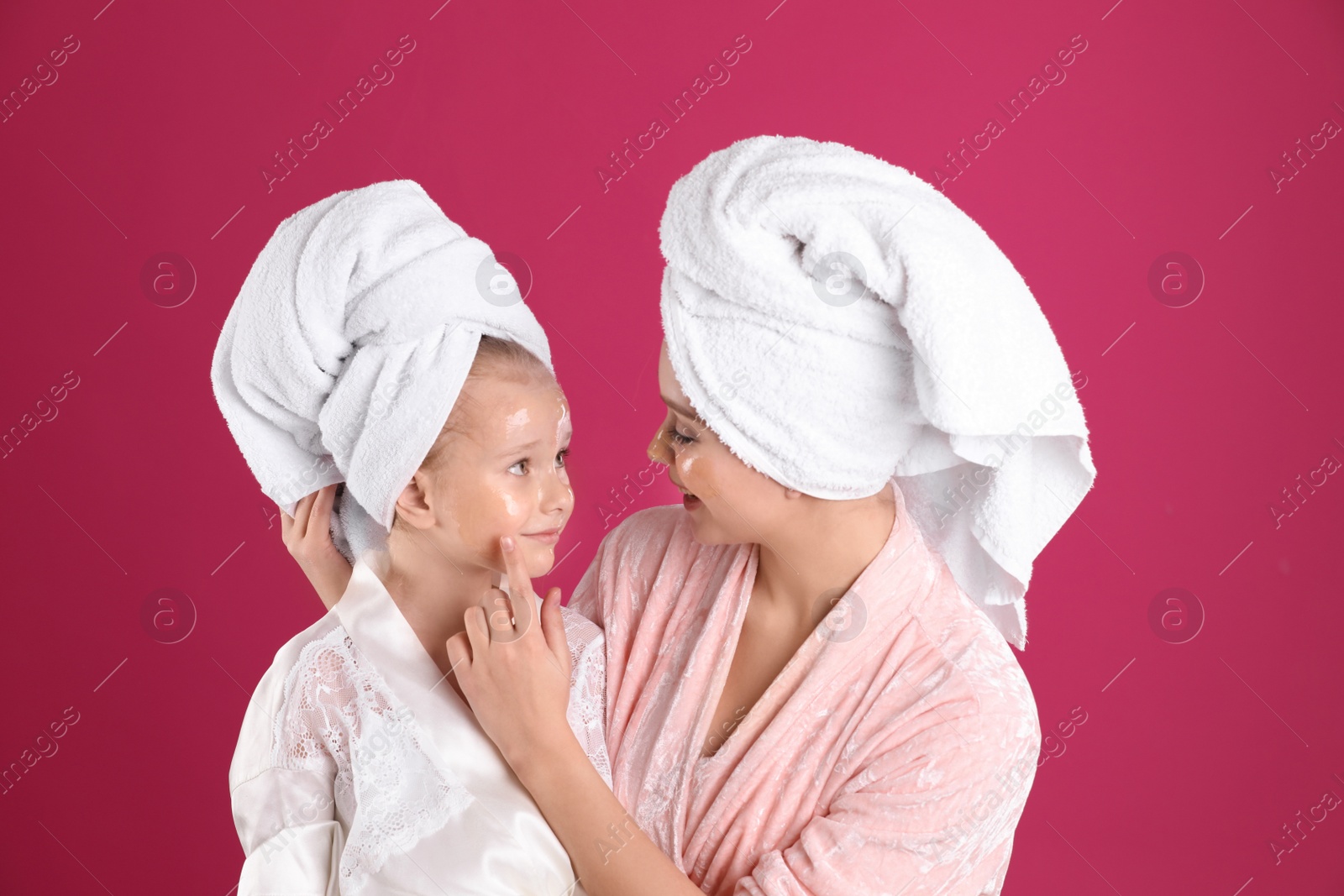 Photo of Happy mother and daughter with facial masks on pink background