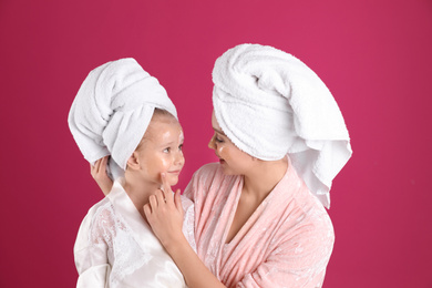 Photo of Happy mother and daughter with facial masks on pink background