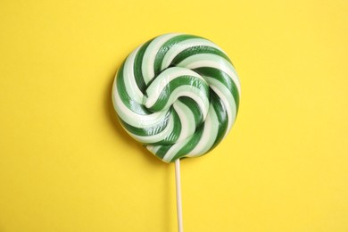 Photo of Stick with colorful lollipop swirl on yellow background, top view