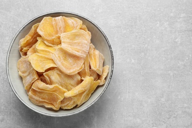 Photo of Delicious dried jackfruit slices in bowl on light grey table, top view. Space for text