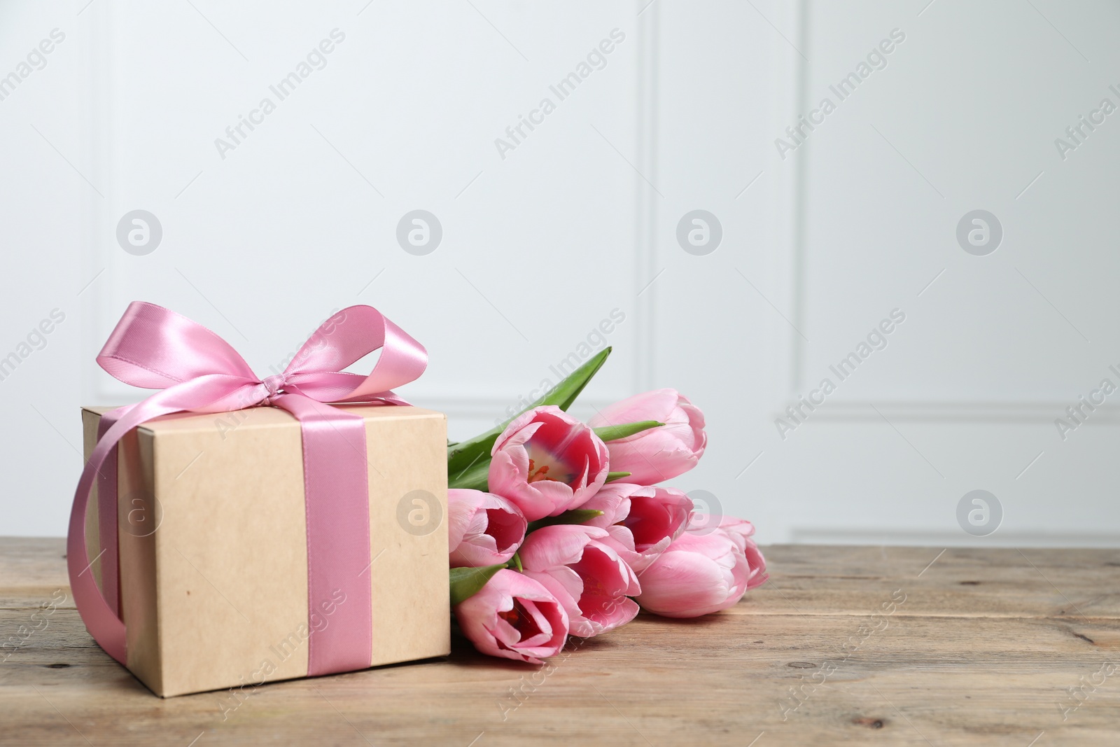 Photo of Beautiful gift box with bow and pink tulips on wooden table. Space for text