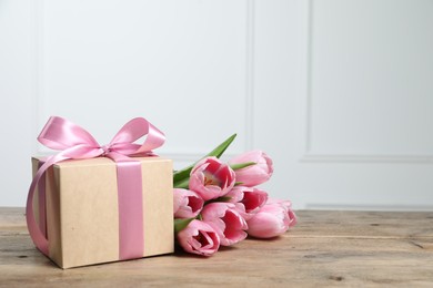 Beautiful gift box with bow and pink tulips on wooden table. Space for text